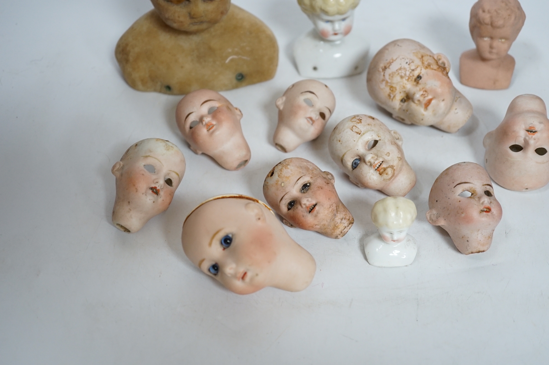 Twelve small bisque doll heads and a wax head